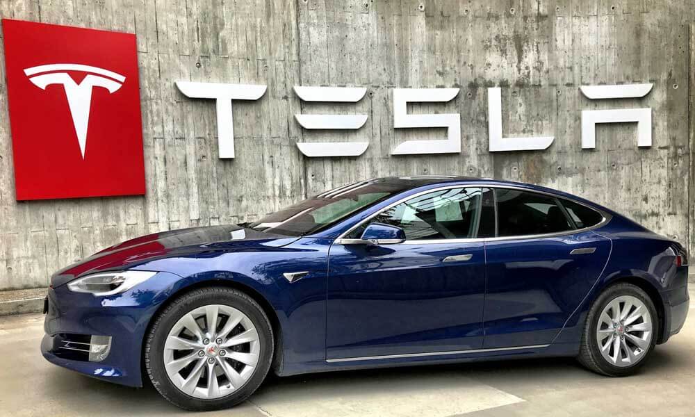 Blue Tesla car in front of company logo