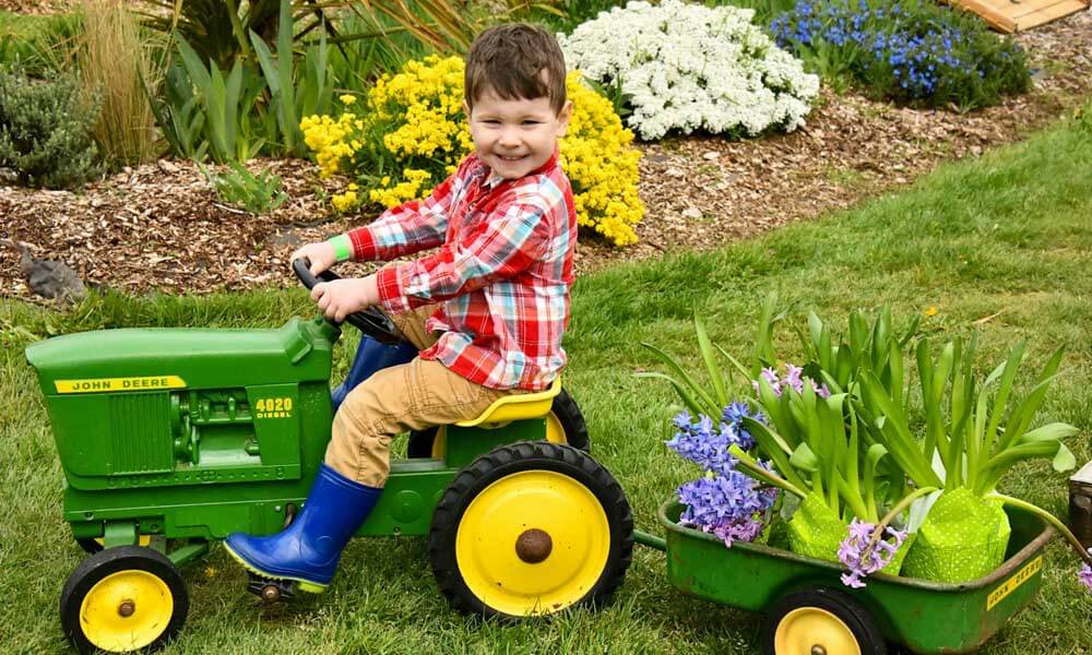 Boy riding small John Deere tractor with classic green and yellow colors