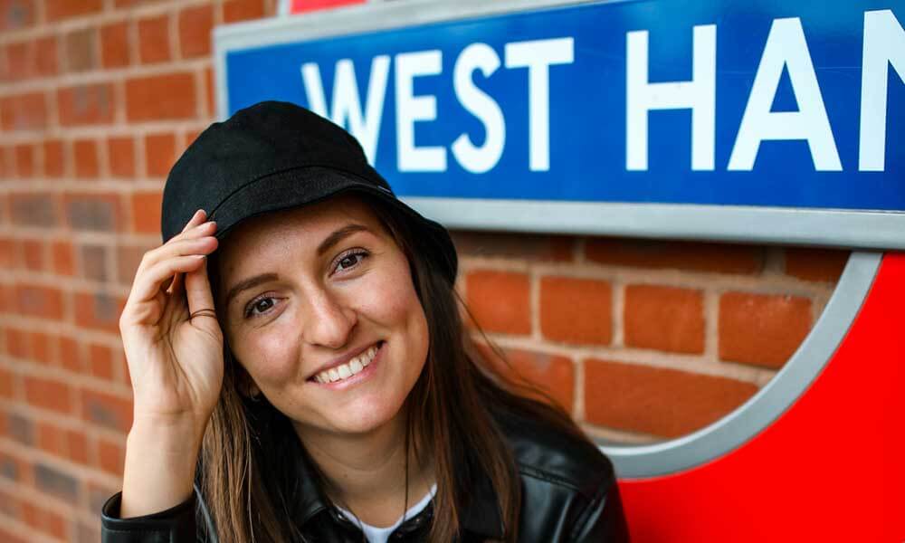 Woman sitting beside West Ham underground station sign